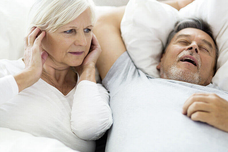 Senior man snoring and woman covering ears