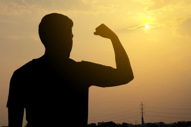 The silhouette of a man, his arms muscles show strong on the background of the sunset.