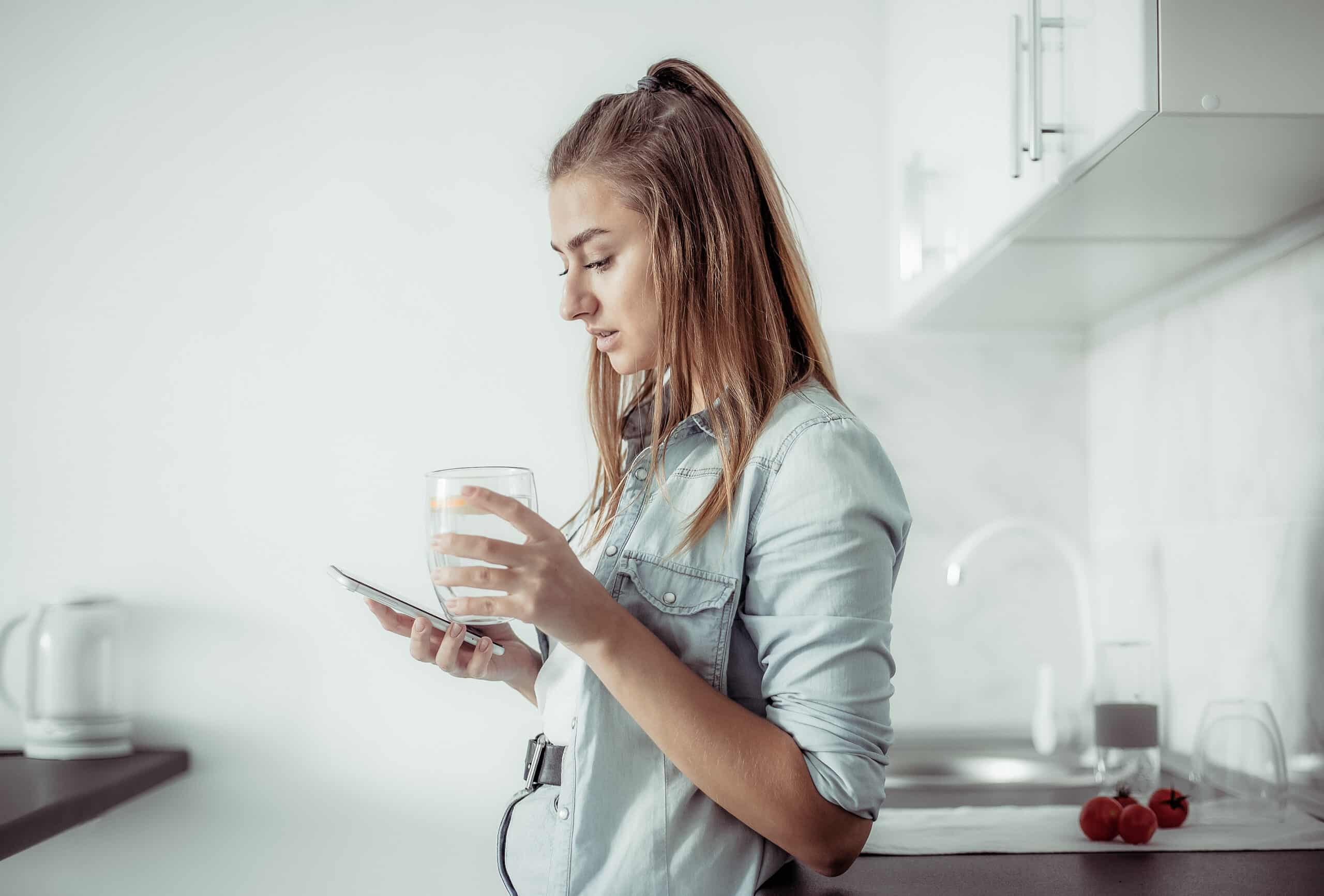Junge Frau steht in der Küche mit einem Smartphone in der Hand