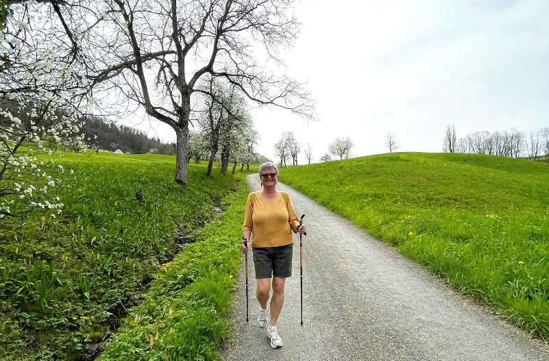 Dame läuft mit Walkingstöcken in der Natur.