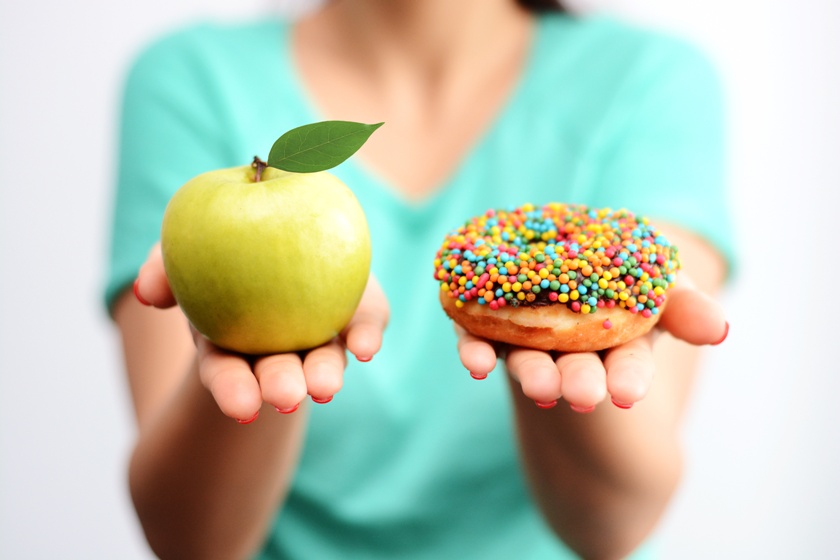 Frau hält in einer Hand einen Apfel und in der anderen ein Donut