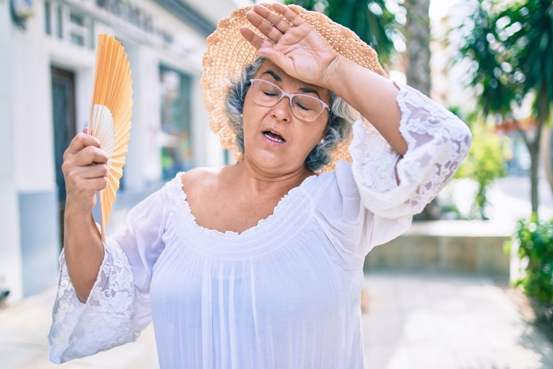 Aeltere Dame fächert sich an einem heissen Tag mit einem Fächer Luft zu