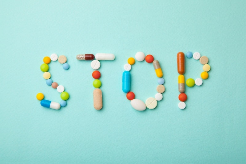 Word STOP from colored pills and capsules on green background. Medicines and tablets kill
