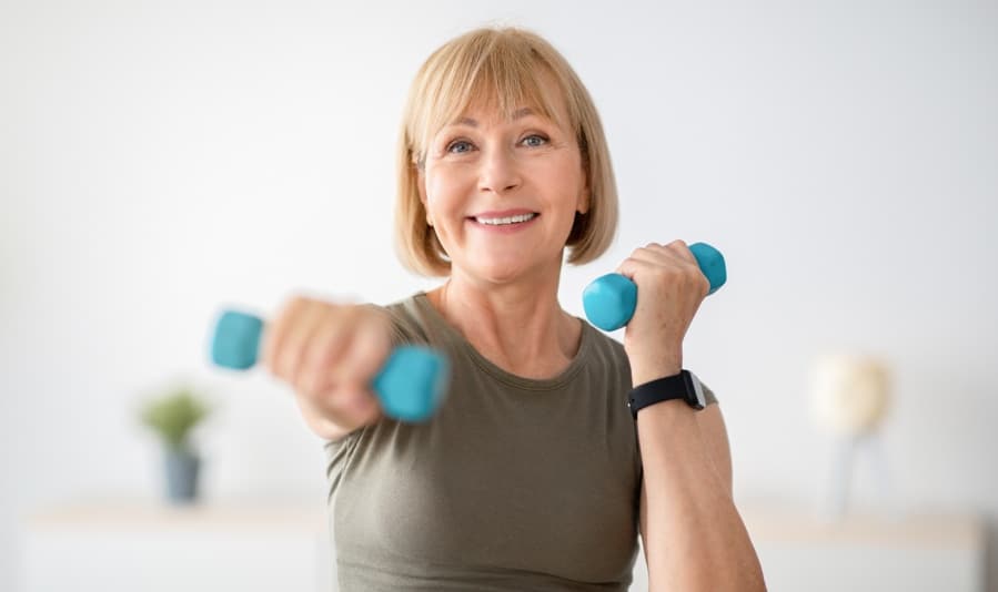 Home training concept. Strong senior woman doing exercises with dumbbells indoors