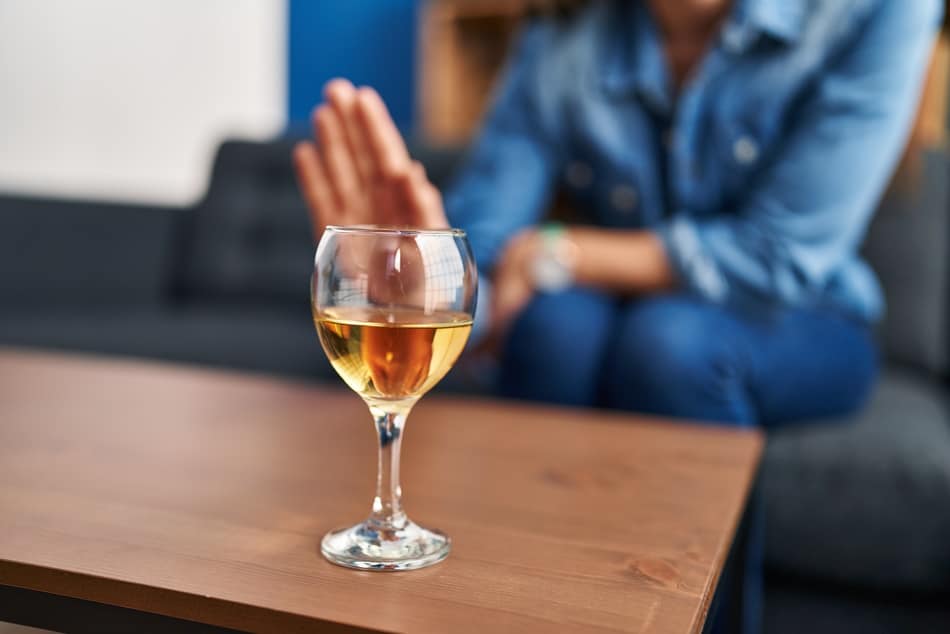 Frau sitzt vor einem Glas Wein und sagt nein zu Alkohol
