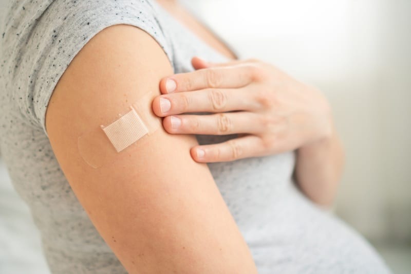 accination of a pregnant woman. Close view of shoulder after vaccine injection with adhesive tape. Covid vaccination concept. Health and medicine during pregnancy.
