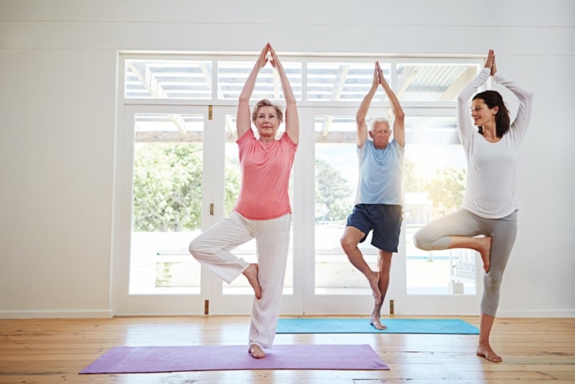 Yoga, tree pose and couple with instructor for fitness, health and retirement wellness in studio. Workout, senior man and woman on mat for pilates, balance or body care exercise together with teacher