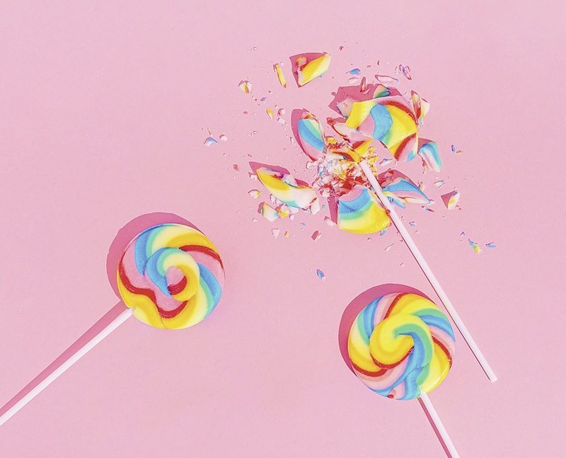 Multi-Colored Whole And Broken Lollipops on pastel pink background, top view. Sugar detox and junk food concept.