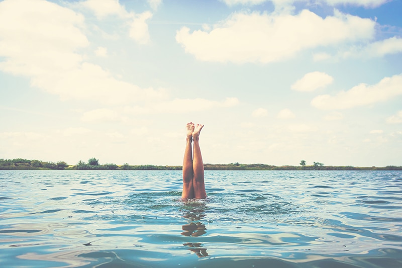 Woman's legs above the water. Unrecognizable woman diving in the sea. Copy space.