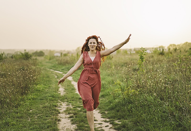 Portraits of a charming red-haired woman with a cute face. Girl posing for the camera in the field at sunset.