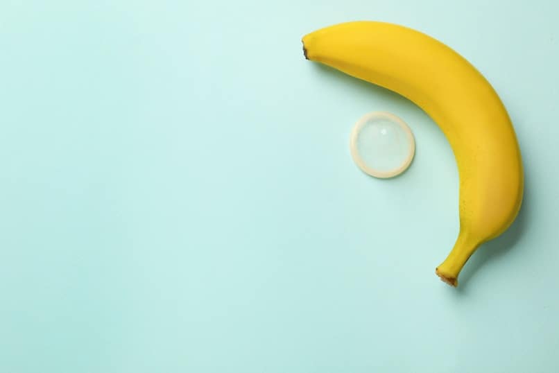 Banana and condom on turquoise background, flat lay with space for text. Safe sex concept