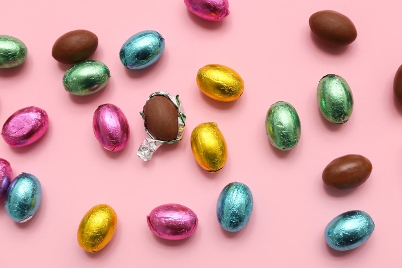 Unpacked and wrapped chocolate Easter eggs in foil on pink background